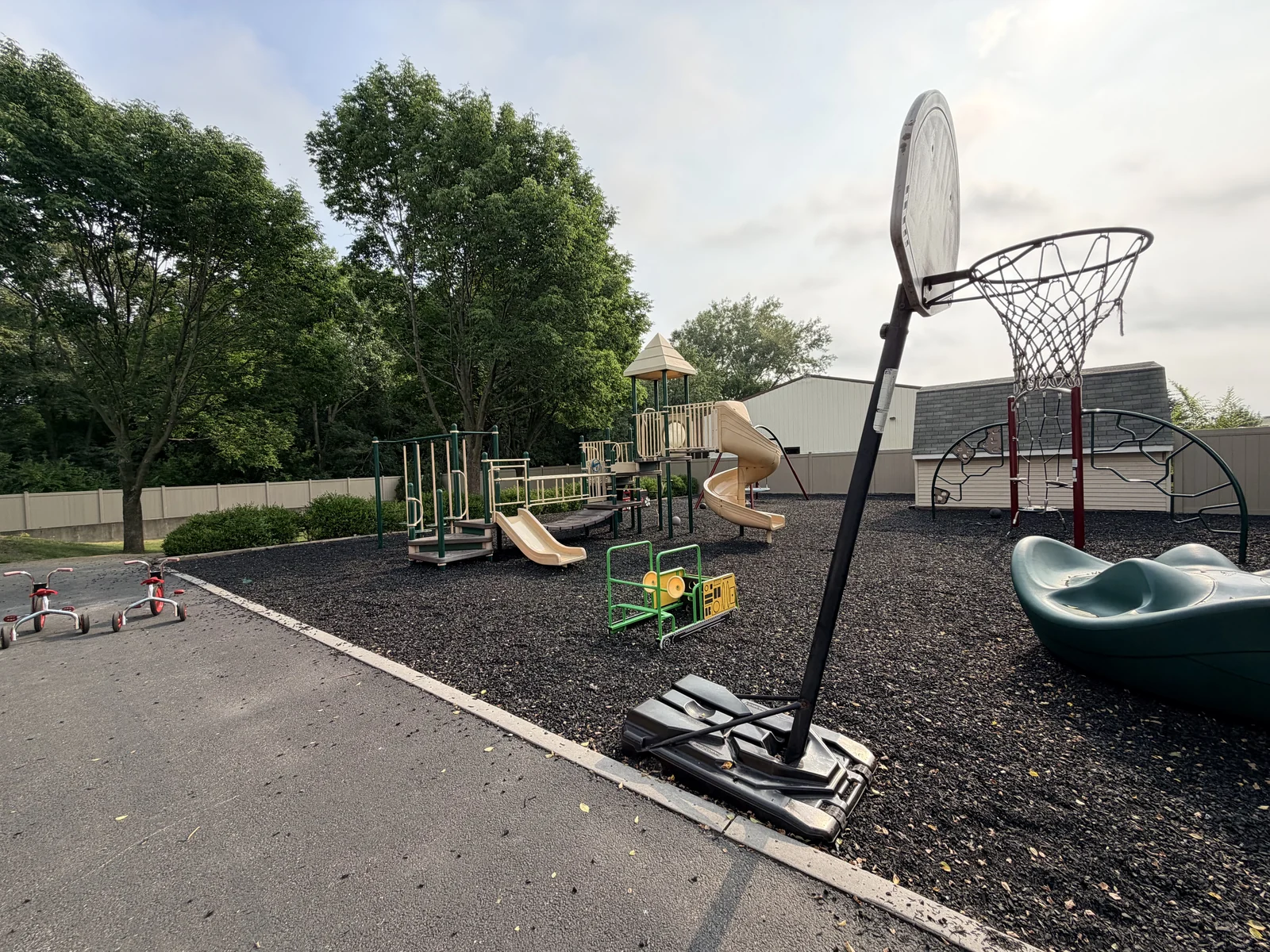 Main playground with slides, climbing structures, a basketball hoop, riding toys, and a fenced boundary