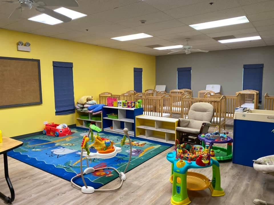 Infant Room floor-play area with activity toys, storage shelves, and cribs