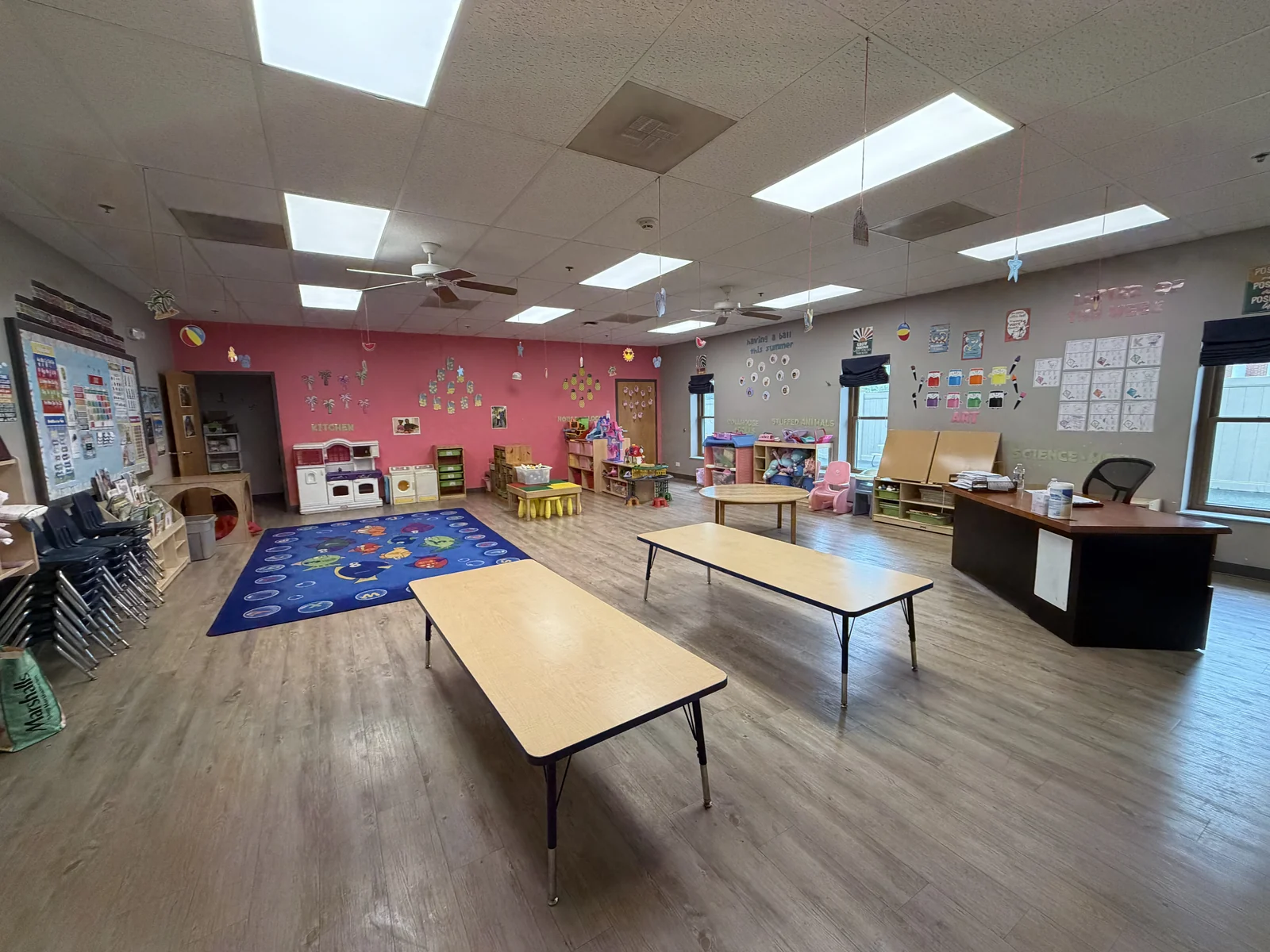 Three-Year-Old Room with child-sized tables, a classroom rug, learning displays, dramatic-play materials, books, and activity centers