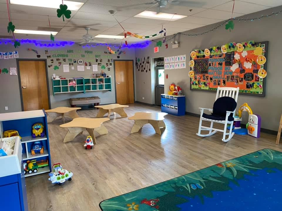 Toddler Room with low tables, toy shelves, a reading area, and classroom displays