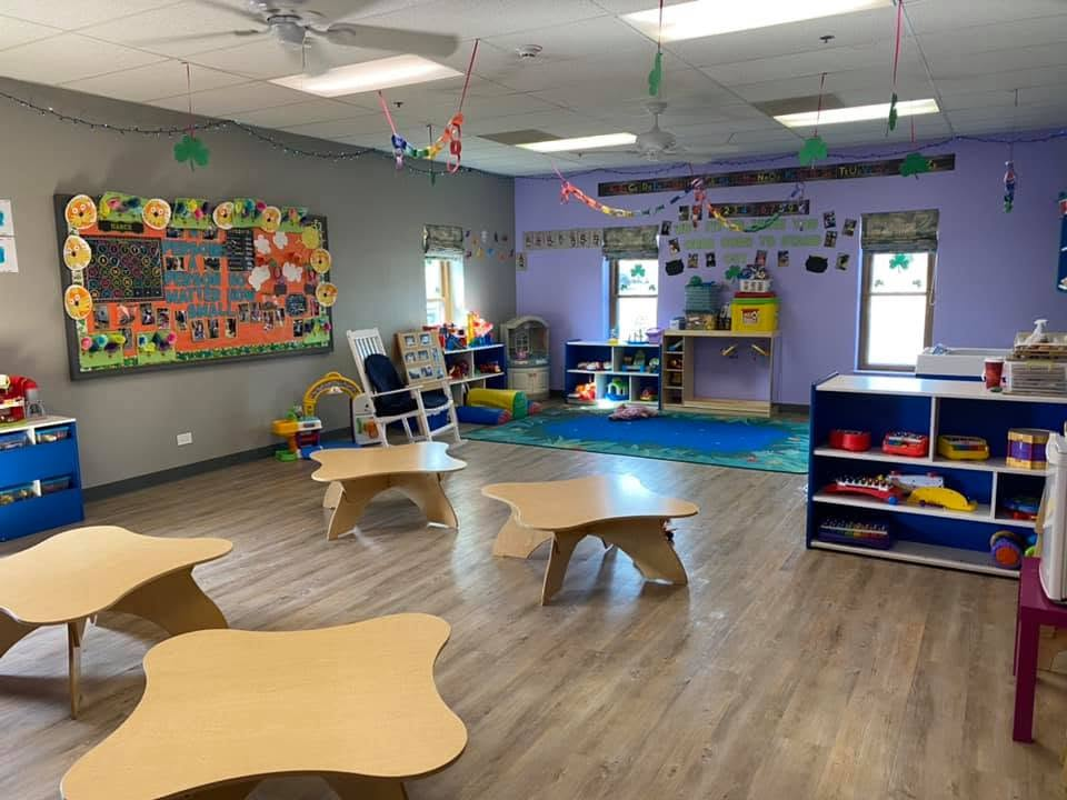 Toddler Room learning and play areas with low tables, shelves, and a classroom rug